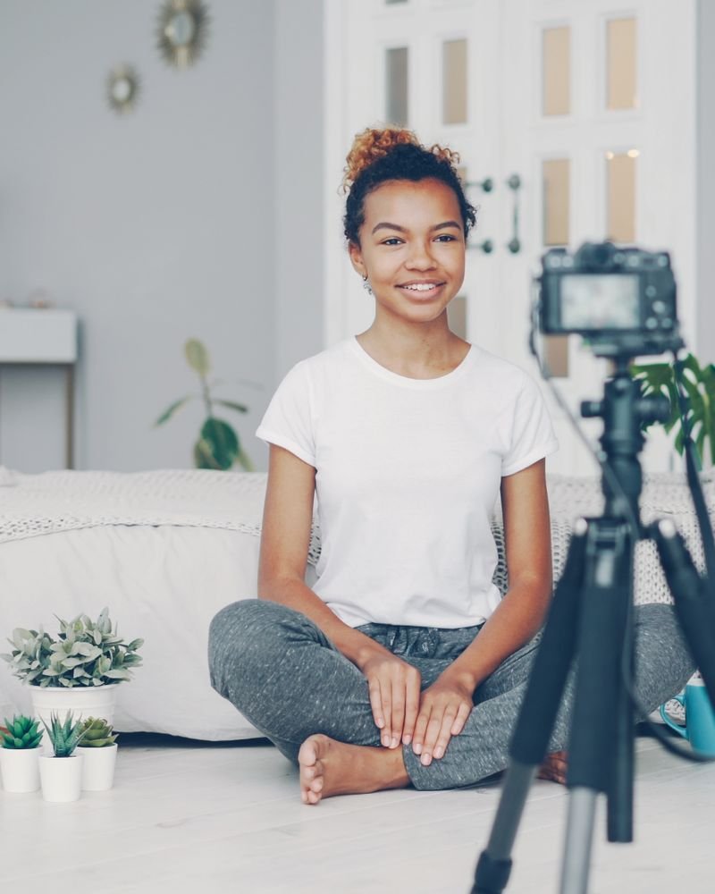A creator filming a seated piece to camera on a tripod in a bright room