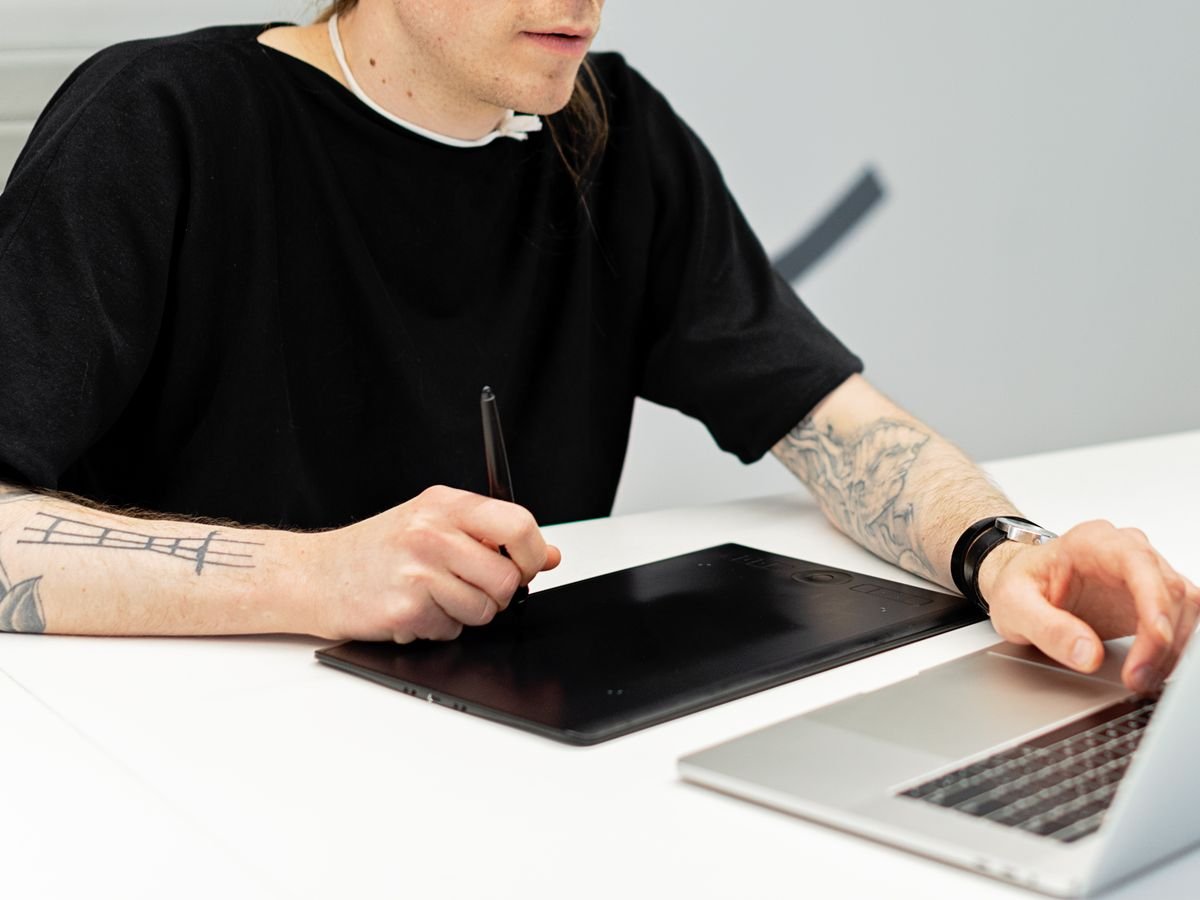 An illustrator drawing on a large graphics tablet beside a laptop